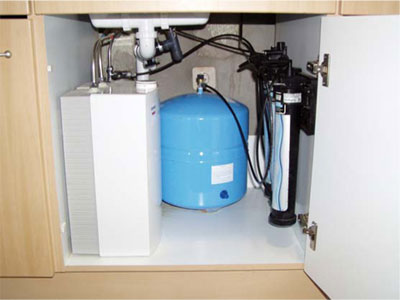 Figur 5. POU omvendt osmose anlæg for nitratreduktion. Placeret under køkkenvask. Til højre ses 3 ens beholdere for partikelfiltrering, aktivt kul filtrering og omvendt osmose. I midten ses 
