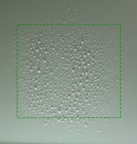 Figur 29. Billede af væskens fladefordeling fra even spray dysen TeeJet TP4001E ved 1,4 bars tryk, en dysehøjde på 35 cm og en fremkørselshastighed på 0,5 m pr. sekund. Kørselsretning er fra billedets top til bund. Dråberne er opsamlet på hvid plastplade og det grønne stiplede kvadrat indikerer en cellestørrelse på 10 x 10 cm.