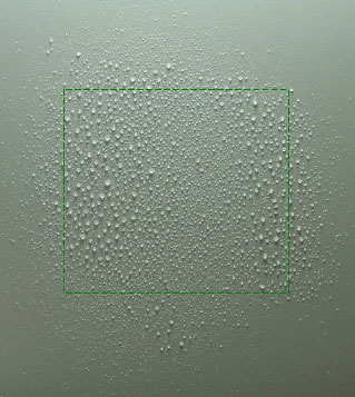 Figur 31. Billede af væskens fladefordeling fra even spray dysen TeeJet TP4001E ved 1,8 bars tryk, en dysehøjde på 35 cm og en fremkørselshastighed på 0,5 m pr. sekund. Kørselsretning er fra billedets top til bund. Dråberne er opsamlet på hvid plastplade og det grønne stiplede kvadrat indikerer en cellestørrelse på 10 x 10 cm.