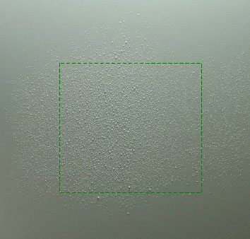 Figur 33. Billede af væskens fladefordeling fra standard fladsprededysen TeeJet TU400033 ved 1,8 bars tryk, en dysehøjde på 35 cm og en fremkørselshastighed på 0,5 m pr. sekund. Kørselsretning er fra billedets top til bund. Dråberne er opsamlet på hvid plastplade og det grønne stiplede kvadrat indikerer en cellestørrelse på 10 x 10 cm.